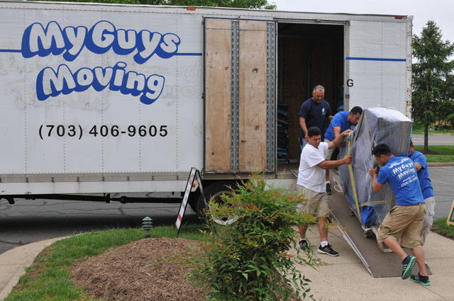mg moving teams carrying a packed piano down a ramp