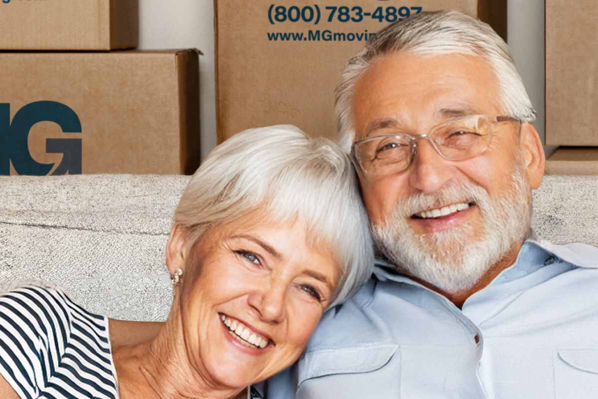 two senior adults sitting on a couch with mg moving boxes in the background