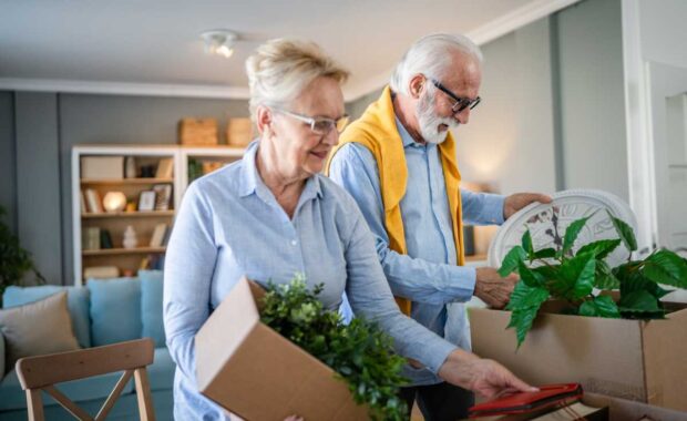 family senior couple man woman husband and wife pensioner grandfather grandmother moving in new apartment taking their stuff belongings and plants in or out of boxes packing or unpacking real people